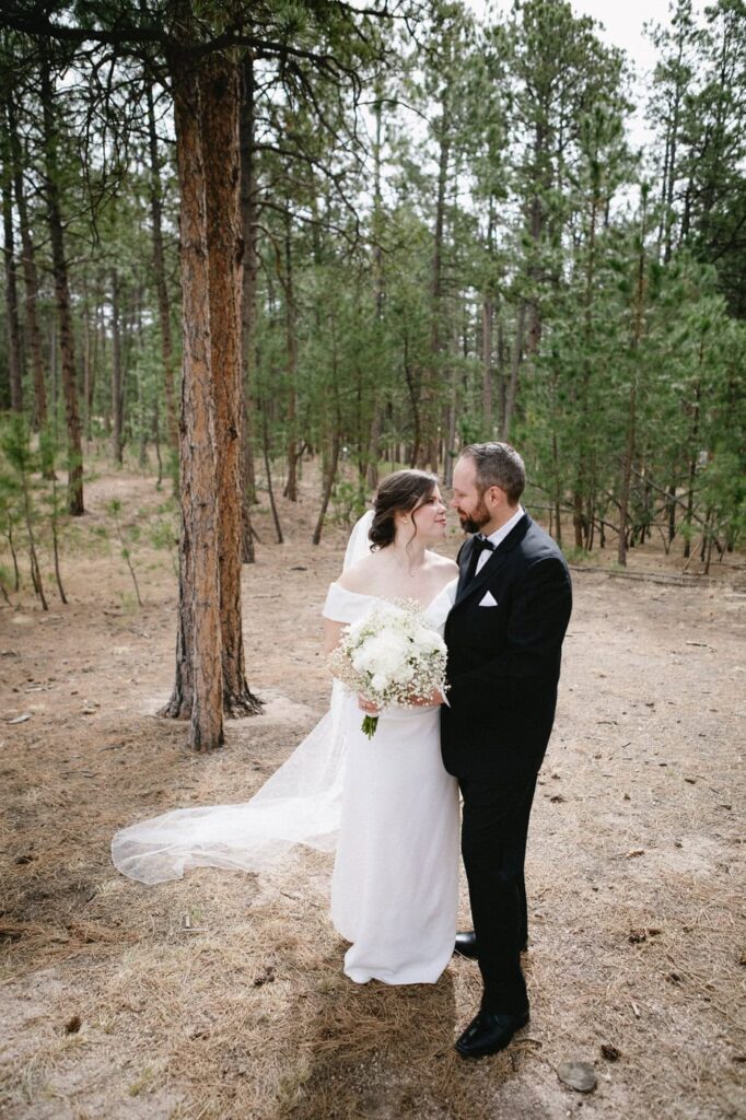 Bride and groom stand by tall pine trees and look at each other