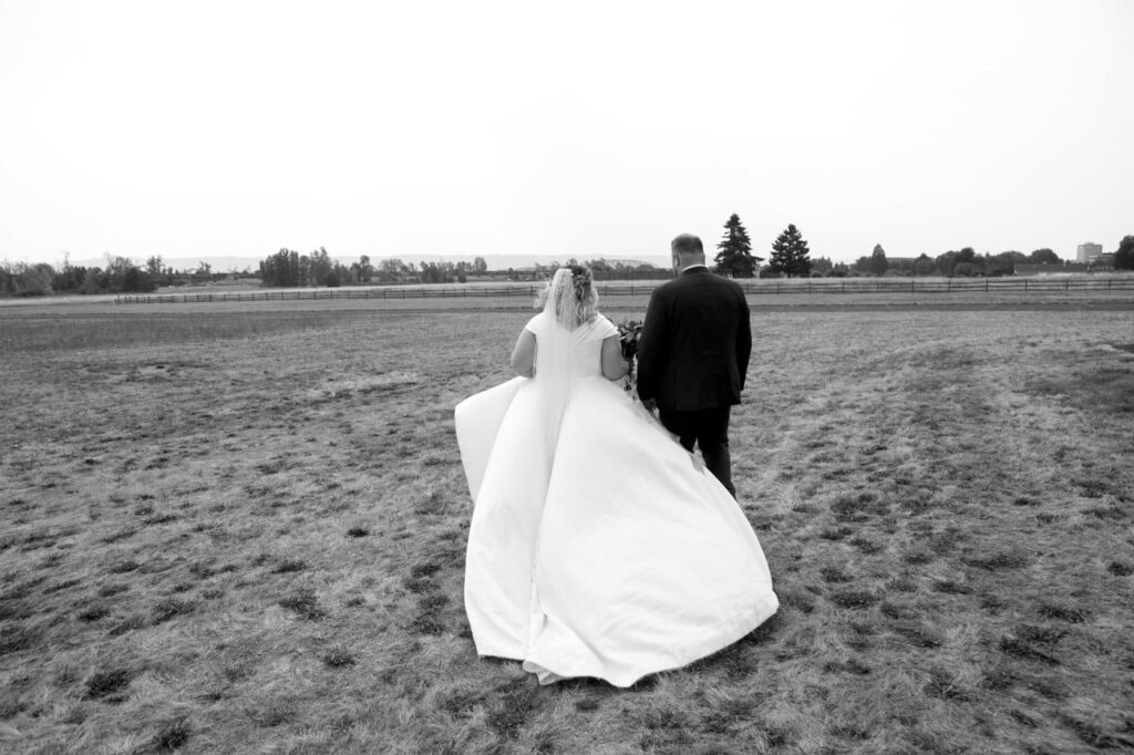 bride with large train walking away from the camera with her groom in a field