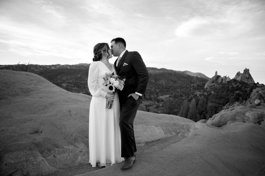 bride and groom atop a red rock kissing