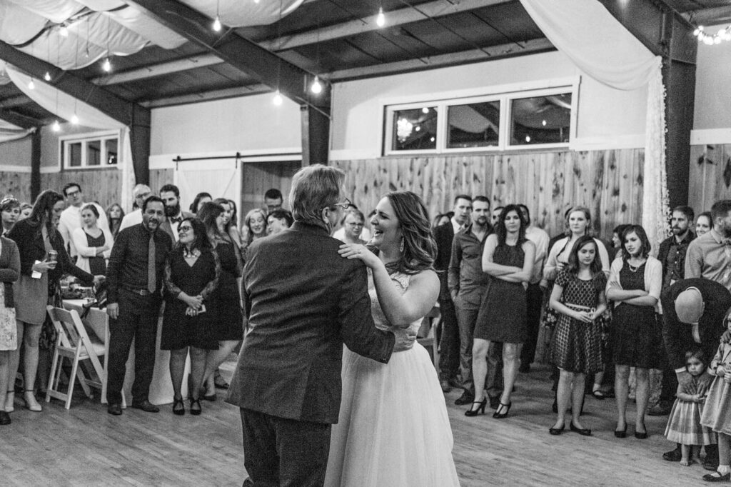 A father and daughter share a dance at the wedding reception as guests look on