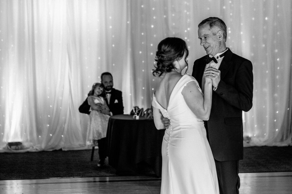 father and daughter share a dance as groom and stepdaughter look on
