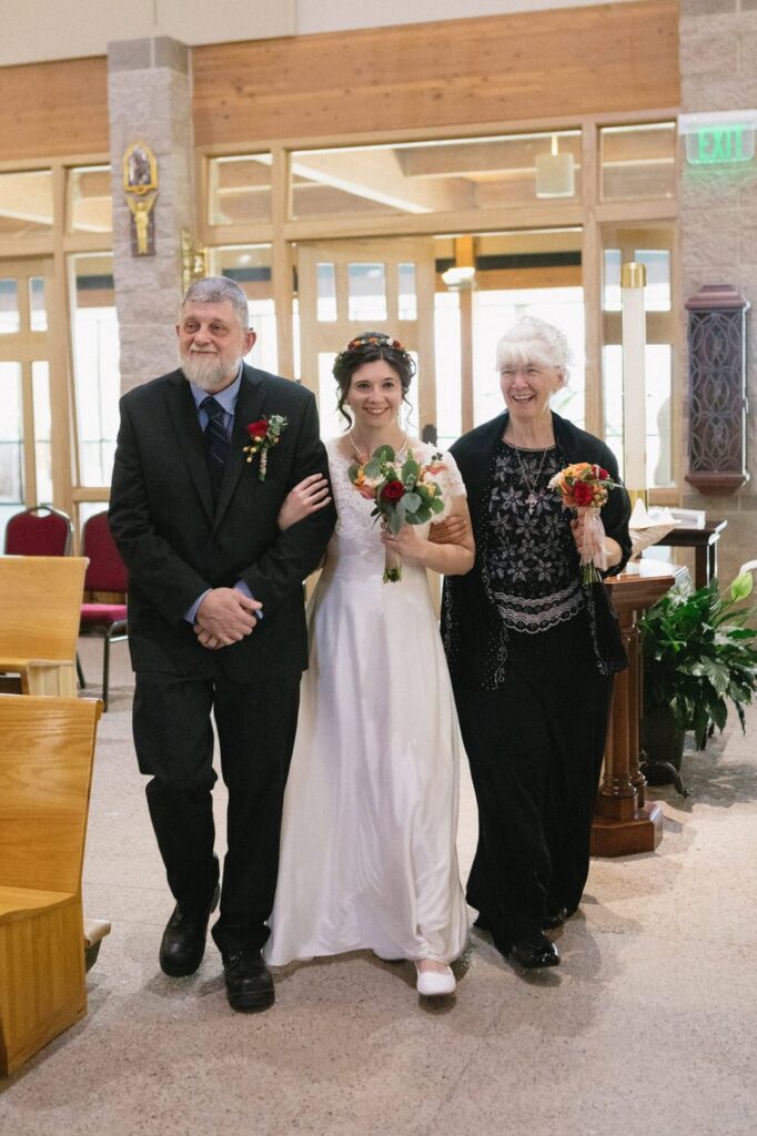 bride walking down aisle with parents at catholic church