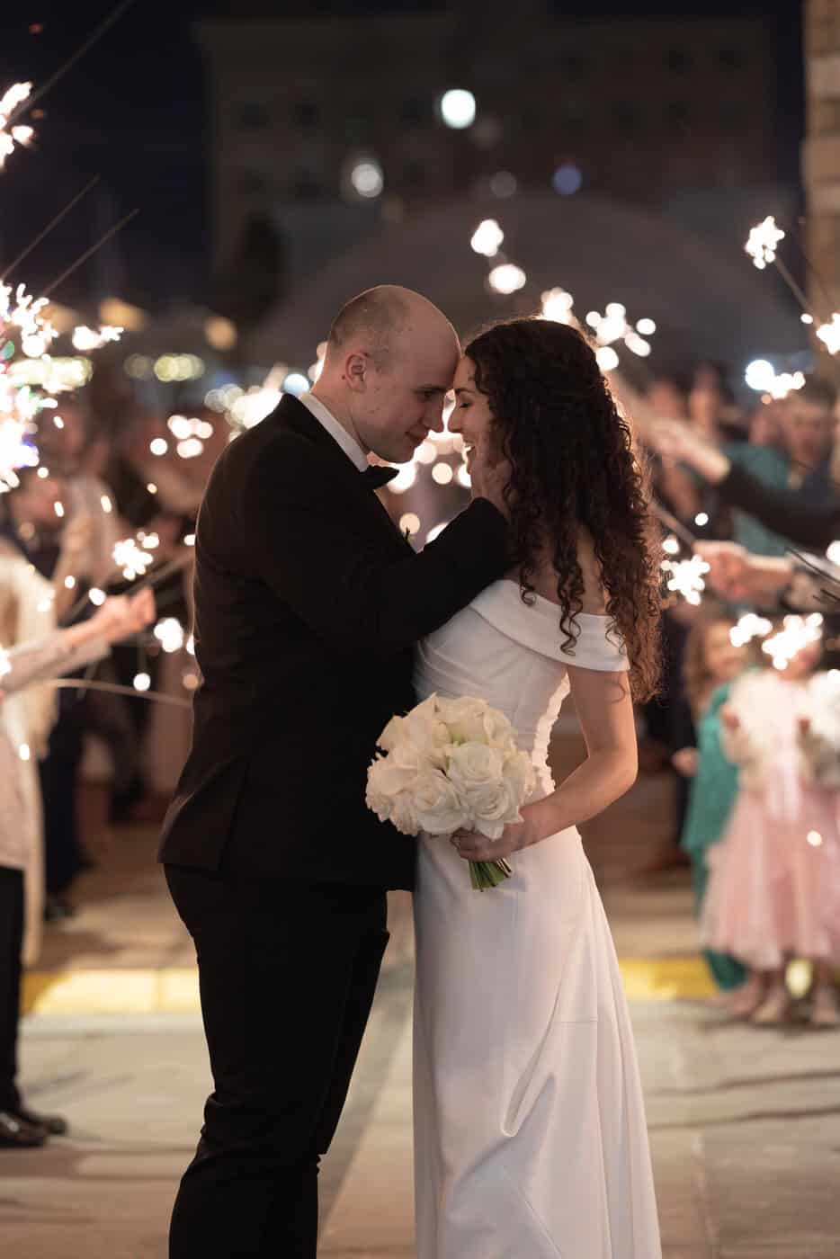 Bride and groom stand foreheads touching during the sparkler grand exit.