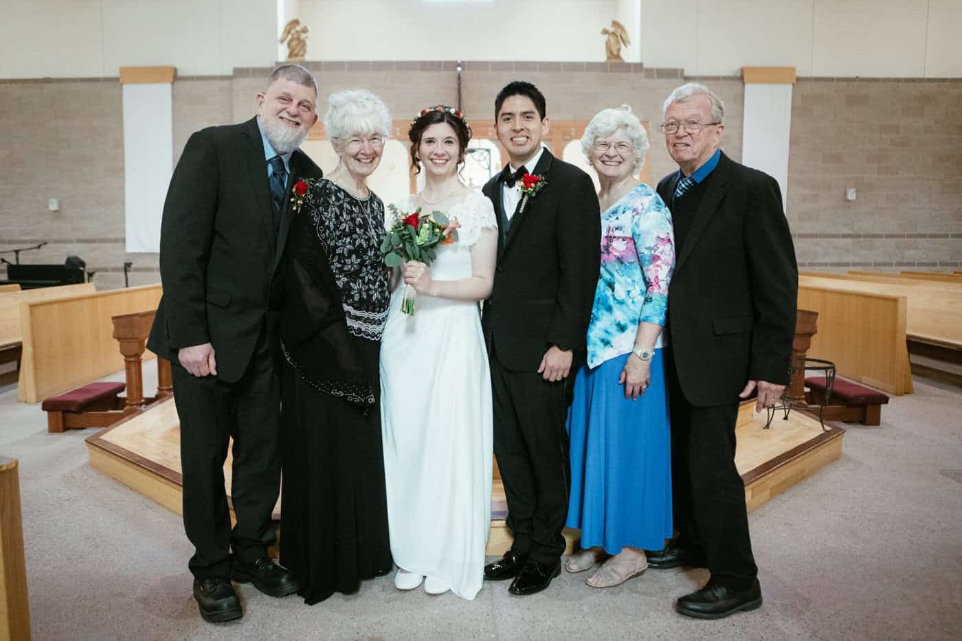 Bride and groom posing with bride's mom and dad and aunt and uncle for a formal photo in the church