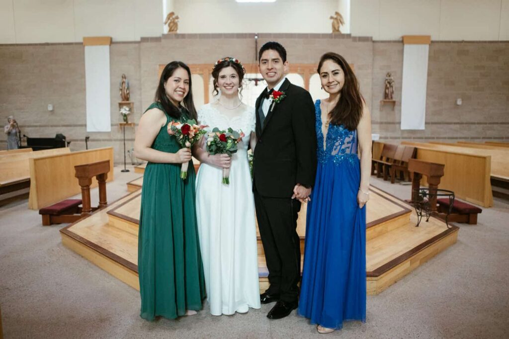 Bride and groom pose with groom's mom and sister in front of church.