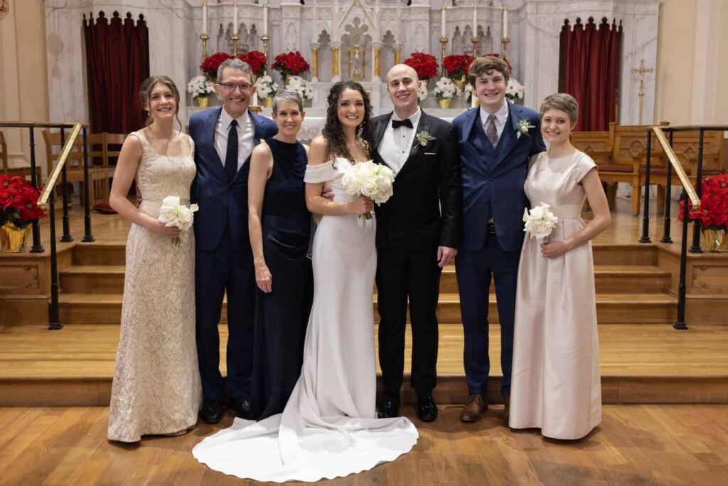 bride and groom posing with bride's family members for a photo in the front of a church.