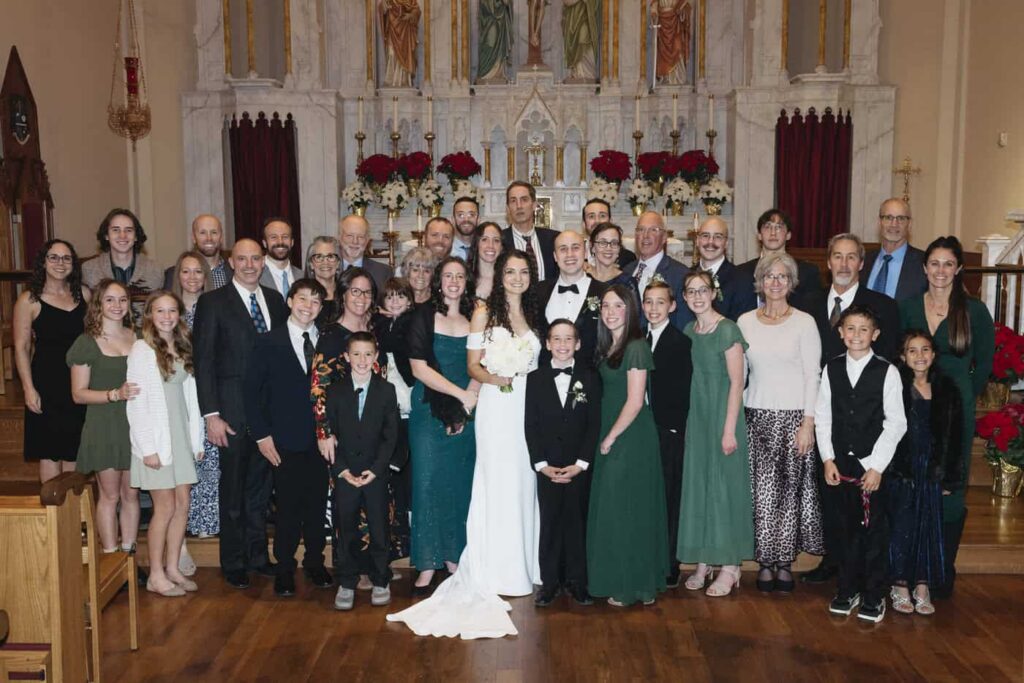 Extended family portrait of bride and groom and lots of family members in the front of a church on their wedding day.